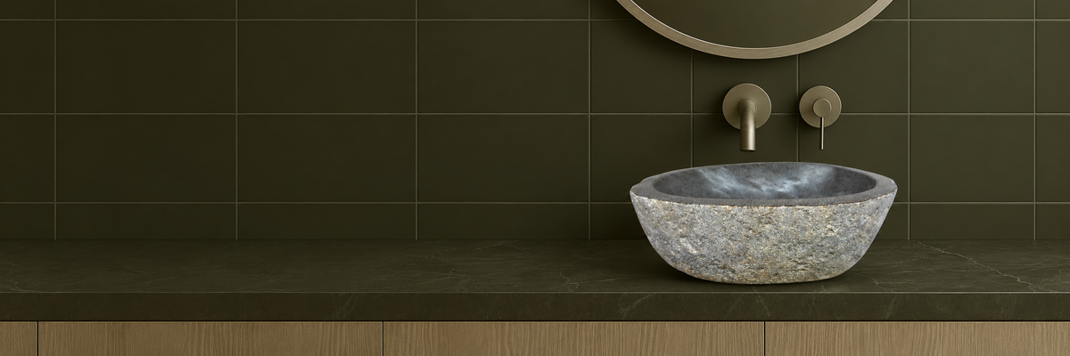 Grey riverstone vanity basin with a textured natural exterior and smooth interior, styled with dark tiles and an oak vanity.